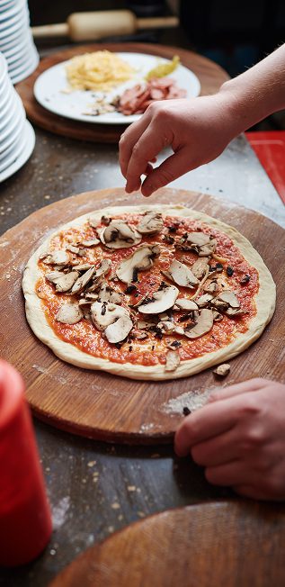Chef's hand adding topping to a pizza at Kelowna pizza restaurant