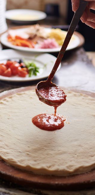 close up of sauce being added to pizza
